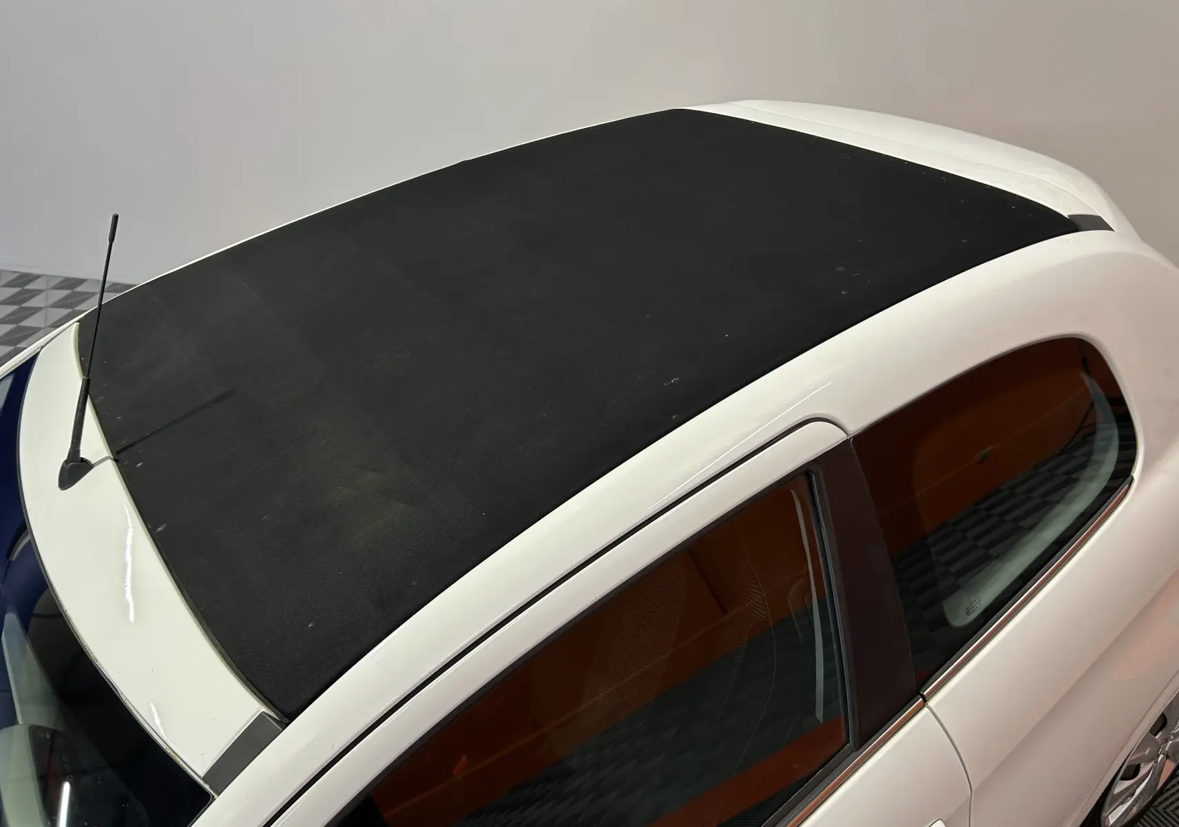 Vue plongeante sur le toit ouvrant en toile noire d'une Peugeot 108 blanche, avec partie latérale droite visible.