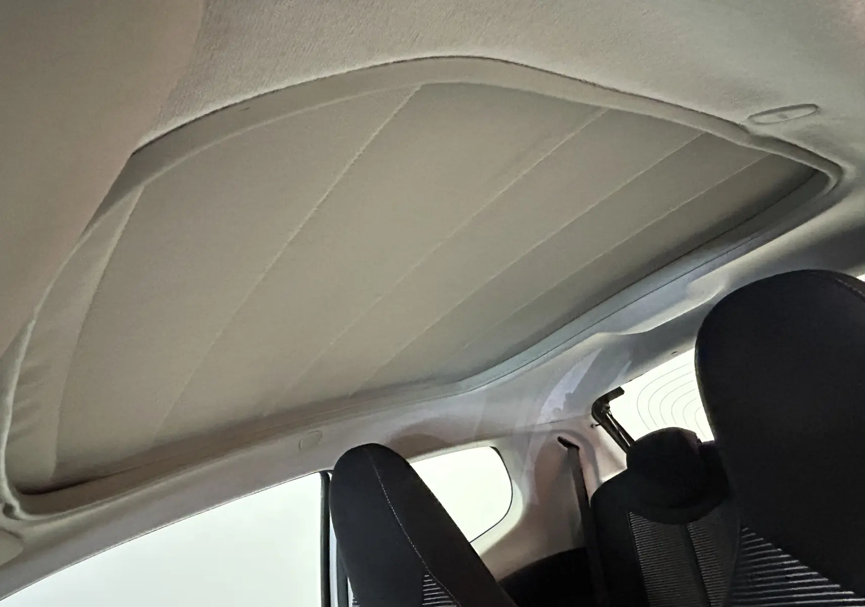 Toit ouvrant en tissu beige vu de l'intérieur arrière d'une Peugeot 108 blanche, sièges noirs visibles.