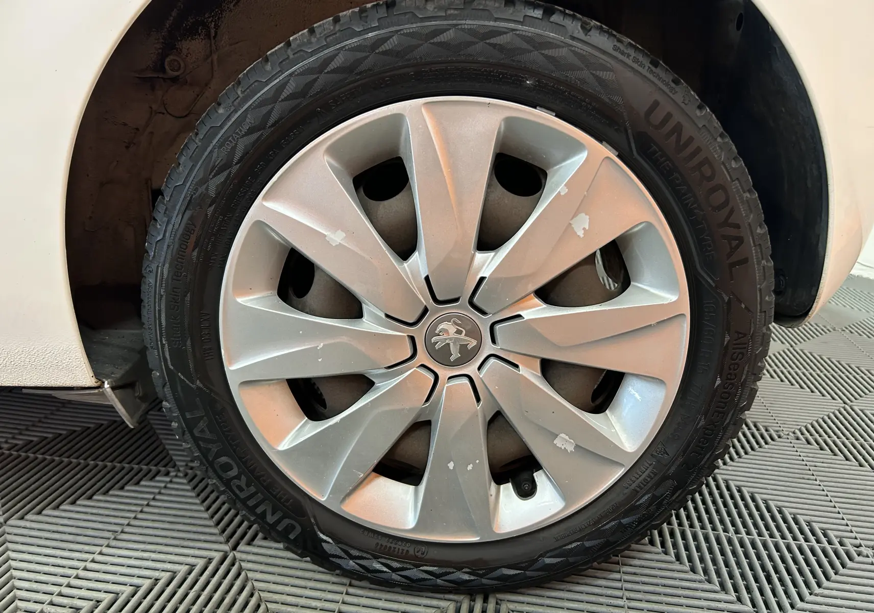 Gros plan sur la roue avant droite d’une Peugeot 108 blanche avec jante argentée et traces d’usure visibles.