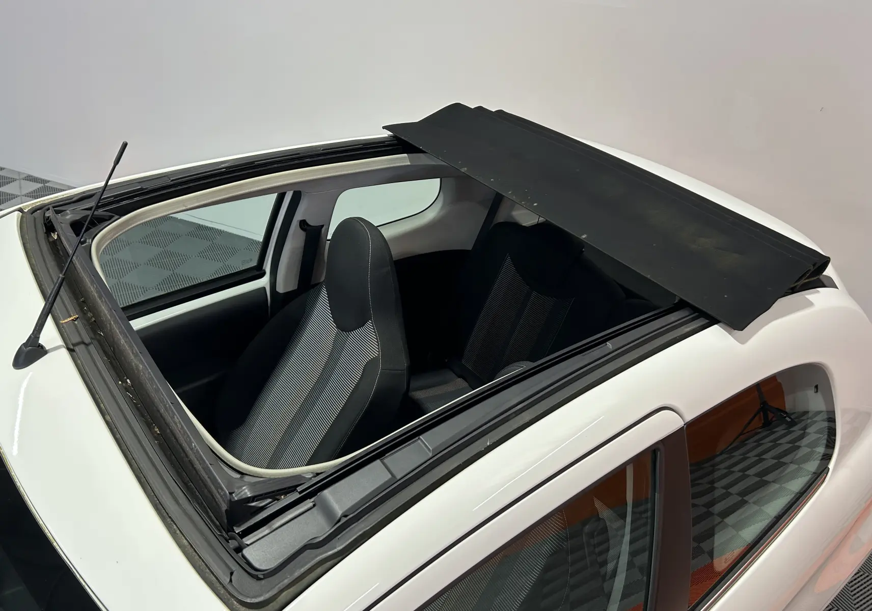 Vue plongeante sur le toit ouvrant ouvert d'une Peugeot 108 blanche, montrant les sièges avant en tissu noir et gris.