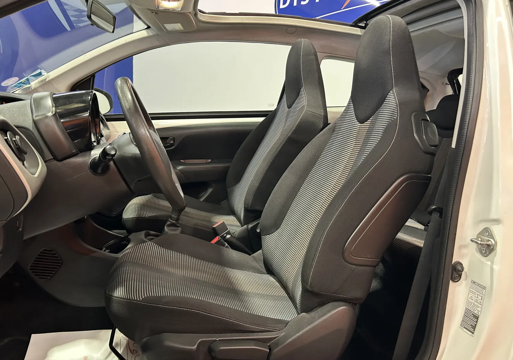Vue intérieure côté gauche montrant les sièges avant en tissu gris et noir d'une Peugeot 108 blanche avec toit ouvrant.