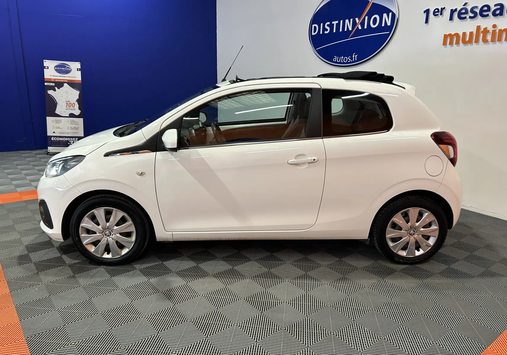Vue latérale droite d'une Peugeot 108 blanche 2014 avec toit ouvrant partiellement ouvert dans un showroom.