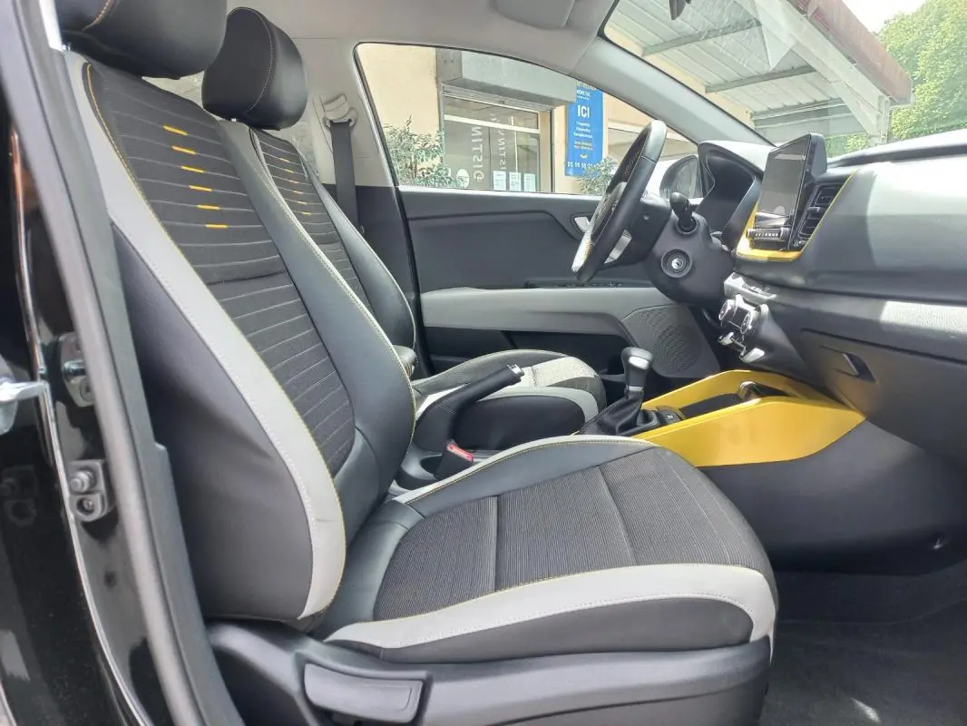 Vue intérieure côté conducteur du Kia Stonic noir 2025, avec sièges noirs et détails jaunes sur la console centrale.
