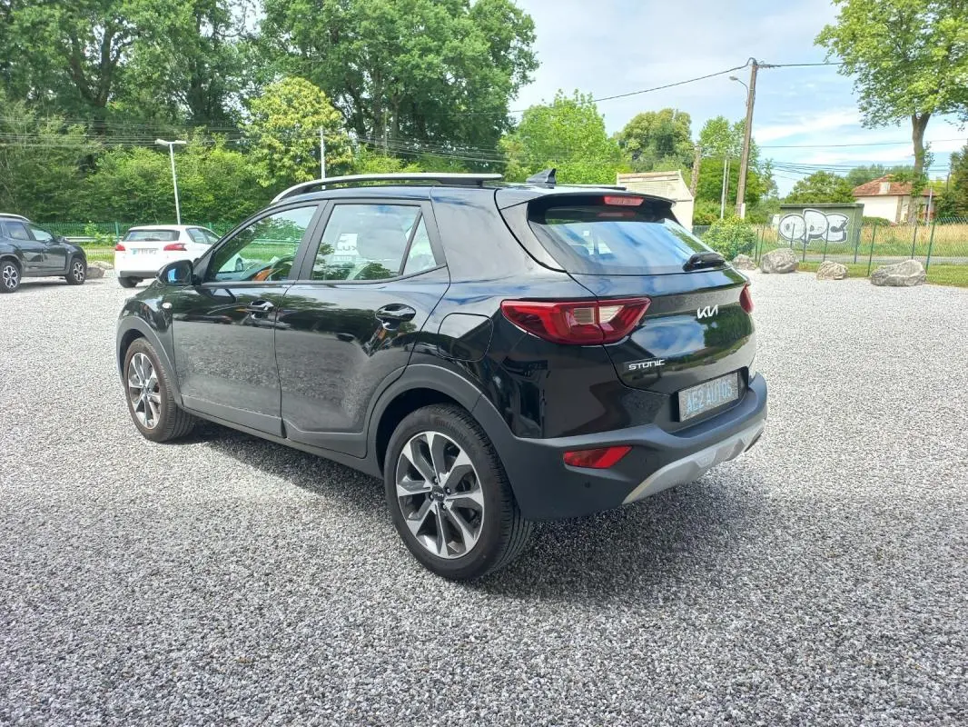 KIA Stonic noir vue 3/4 arrière droit, avec jantes alliage et toit avec barres de toit visibles.