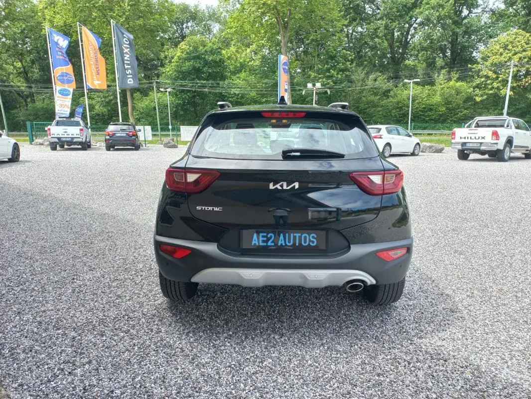 Vue arrière d’un KIA STONIC noir 2025 avec feux arrière distinctifs et plaque AE2 AUTOS sur parking gravillonné.
