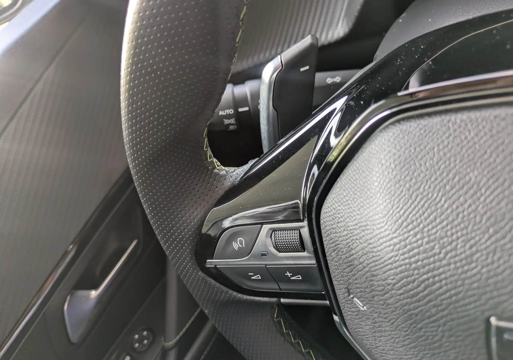 Gros plan sur la partie gauche du volant en cuir perforé noir avec surpiqûres vertes du Peugeot 208 Hybrid 145 GT 2025.