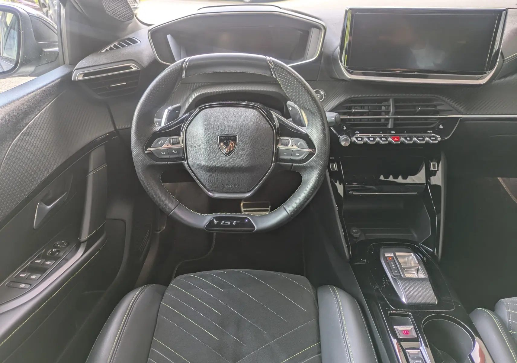 Vue intérieure frontale du poste de conduite de la Peugeot 208 Hybrid 145 GT avec volant GT et sellerie Alcantara noire surpiquée verte.