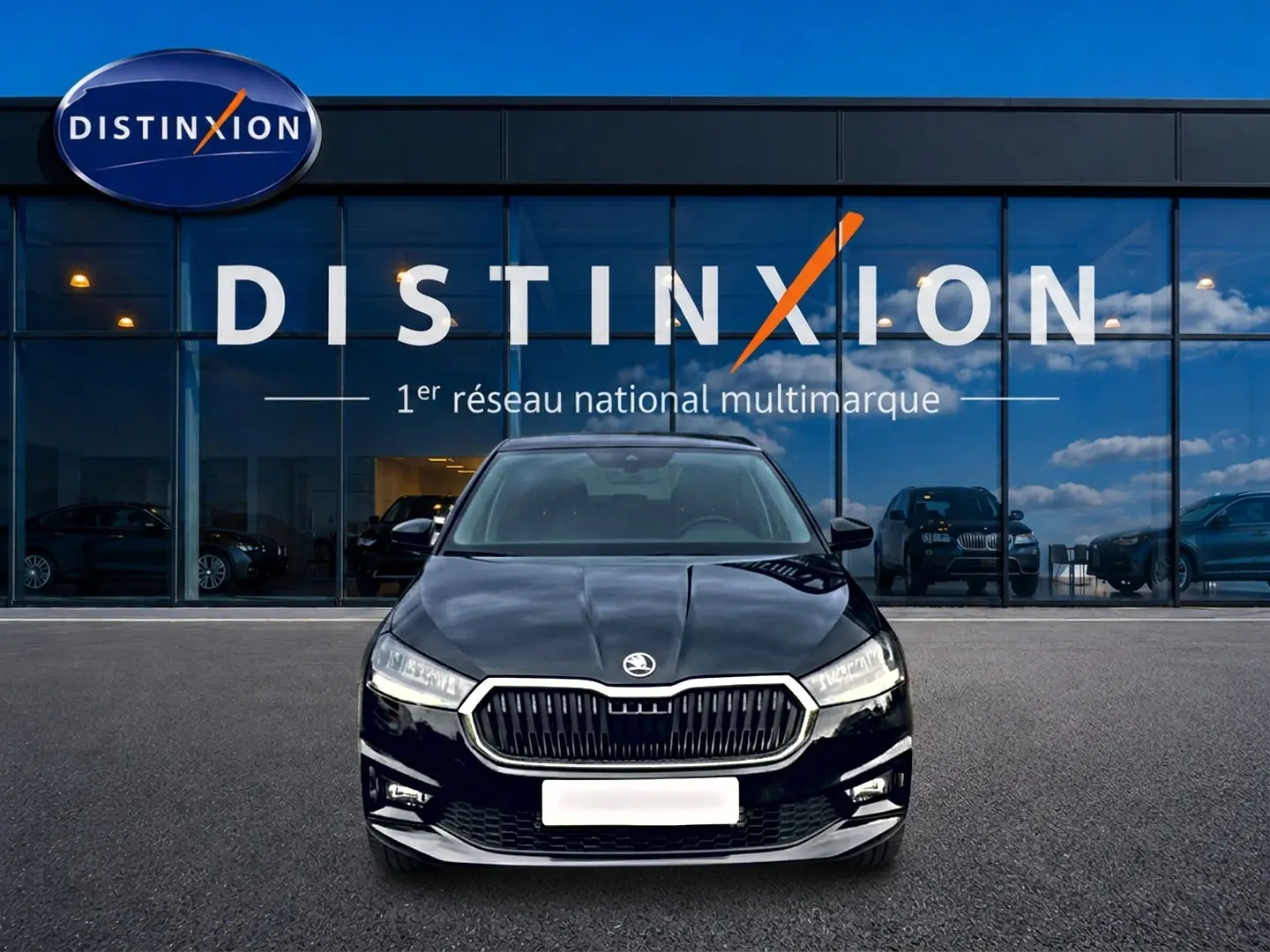 Vue frontale d'une Skoda Fabia noire 2025 garée devant une vitrine avec logo Distinxion en arrière-plan.