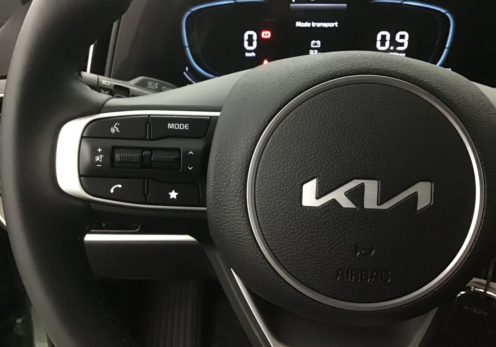 Gros plan sur le volant cuir du Kia Sportage 2025 avec commandes intégrées et tableau de bord digital lumineux.