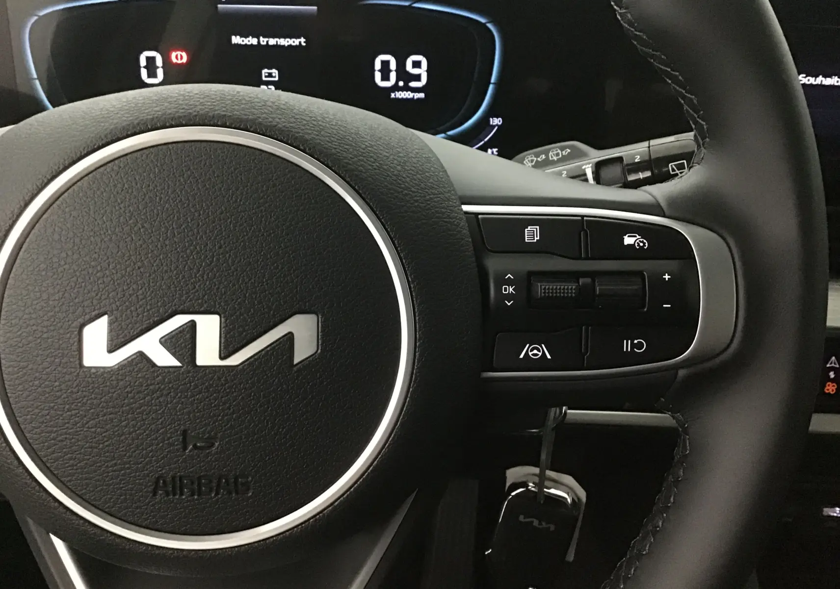 Gros plan sur le volant cuir du Kia Sportage 2025 avec commandes multifonctions et tableau de bord digital lumineux.