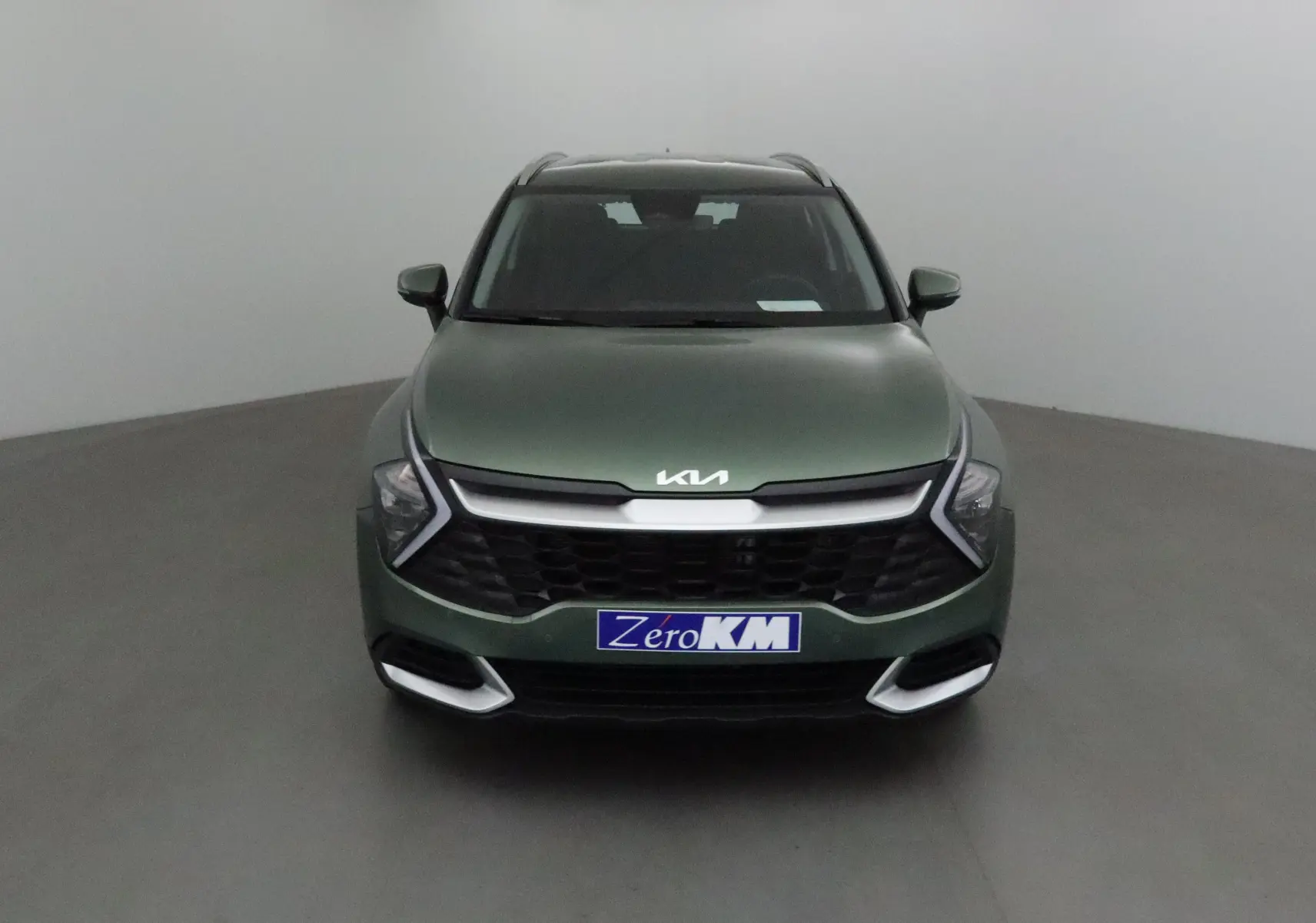 Vue frontale d'un KIA SPORTAGE 2025 vert Borneo avec calandre noire et phares LED en forme de flèche.