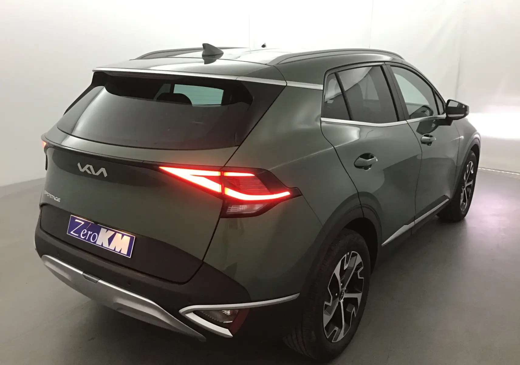 Vue 3/4 arrière droite du Kia Sportage 2025 vert Borneo avec feux LED allumés et jantes alliage noires.