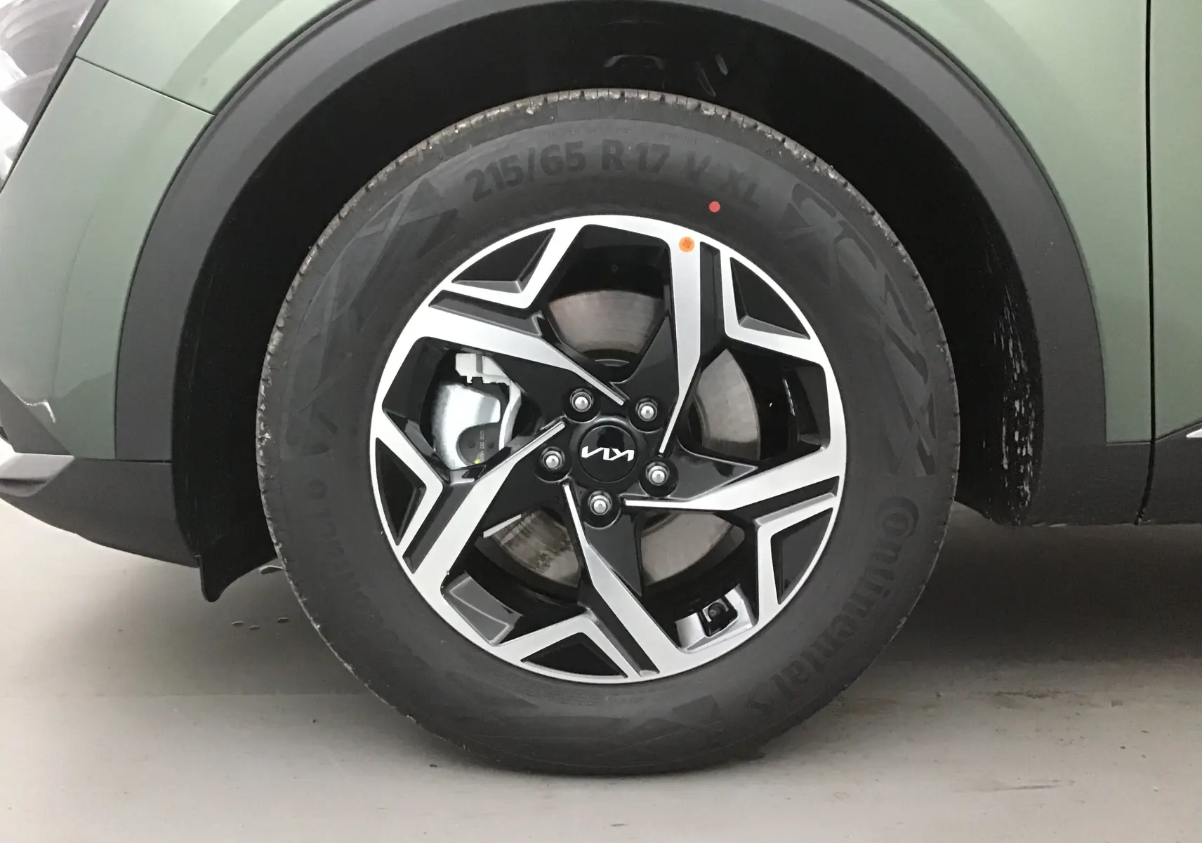 Gros plan sur la roue avant gauche du Kia Sportage 2025 vert Borneo avec jante alliage noire et argentée au design moderne.