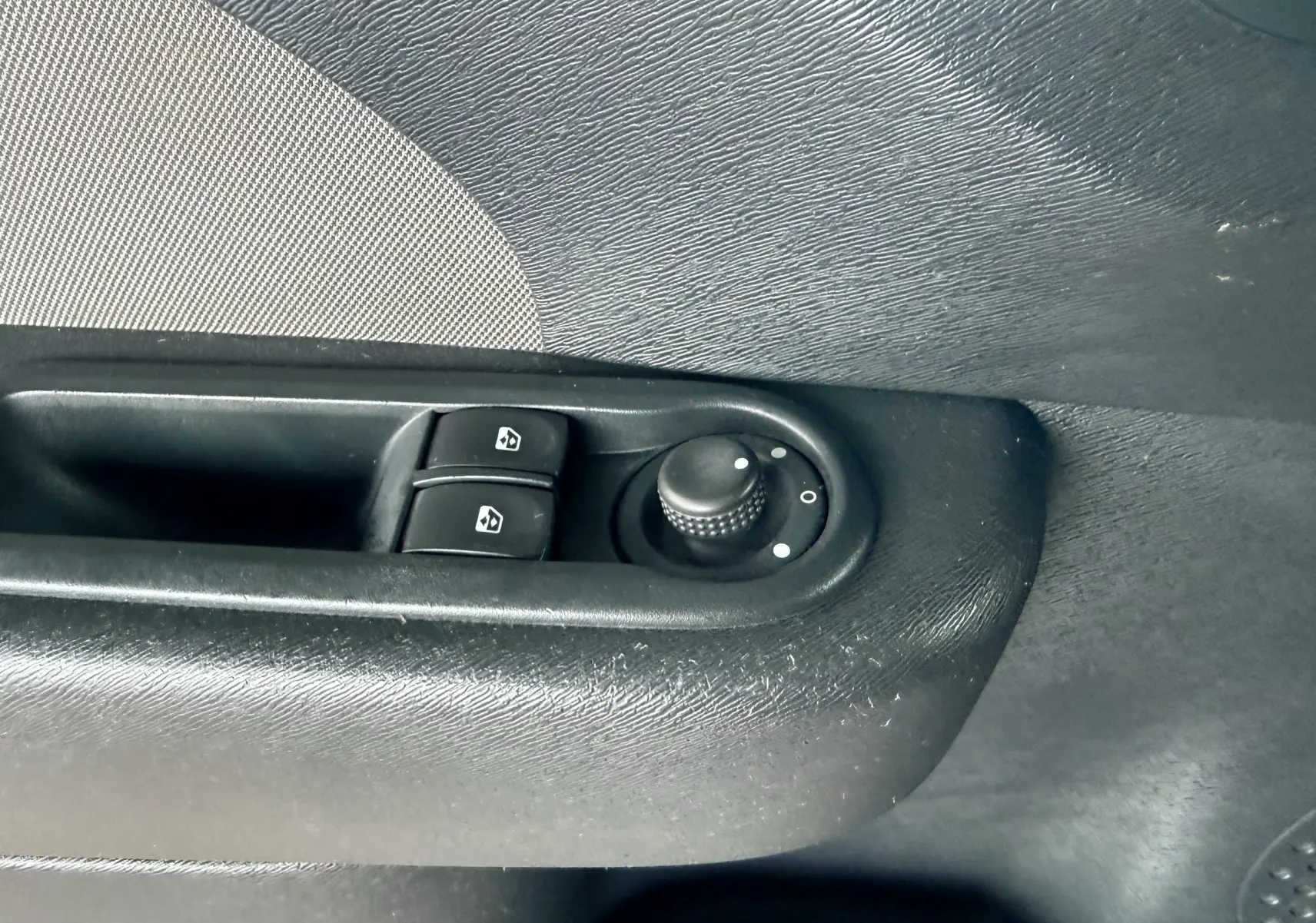 Gros plan sur les commandes de lève-vitres et réglage des rétroviseurs côté gauche d’une Renault Twingo II gris.