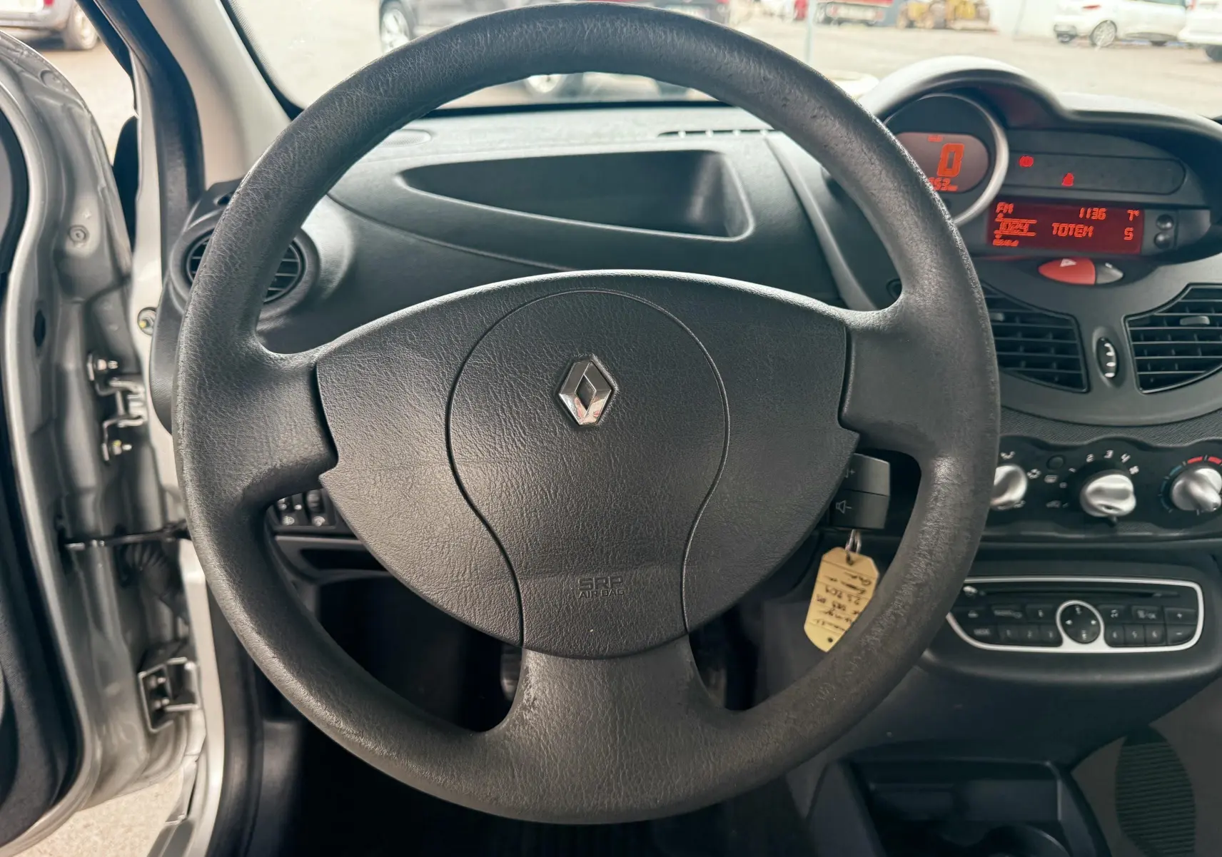 Vue intérieure centrée sur le volant noir de la Renault Twingo II gris, avec tableau de bord et commandes visibles.