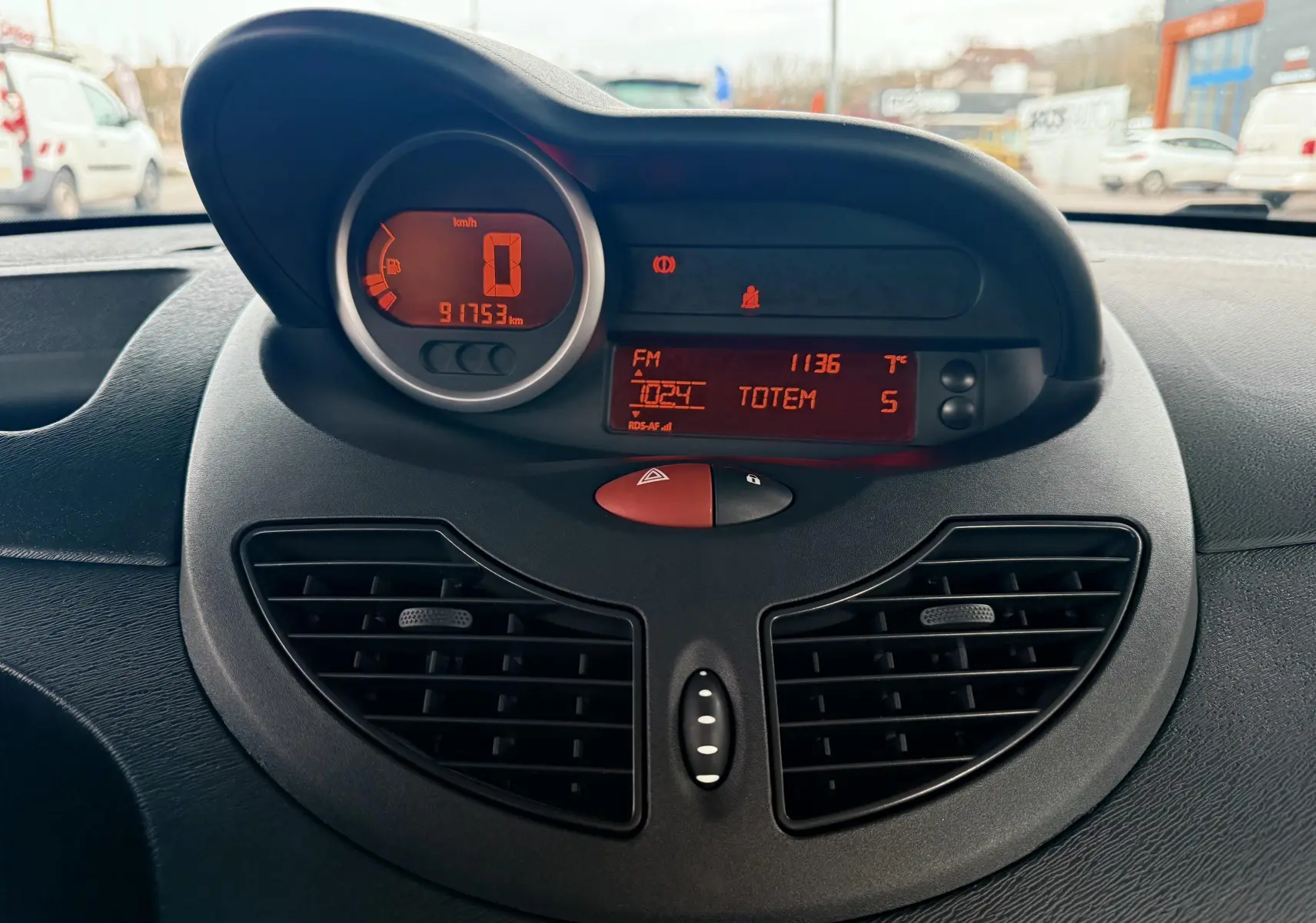 Tableau de bord de Renault Twingo II gris de 2009, affichage digital orange avec compteur et radio FM visible.