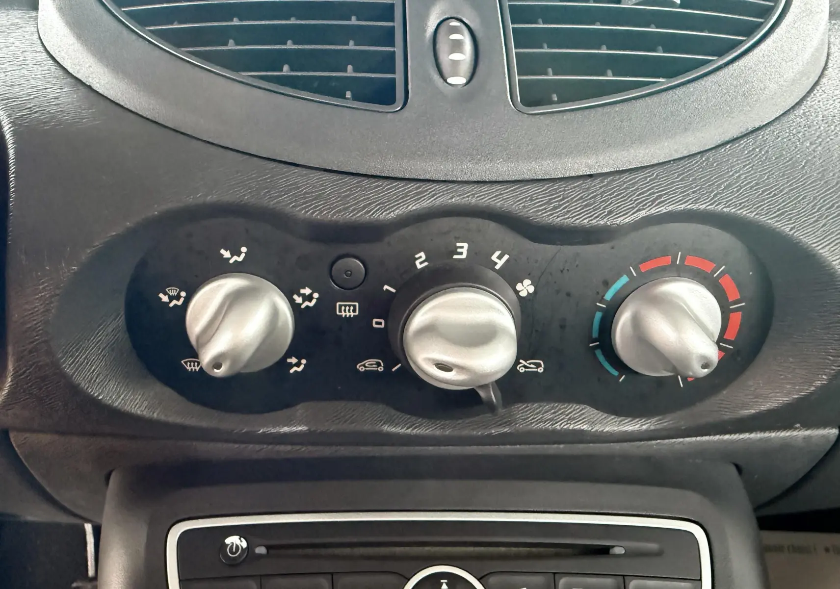 Gros plan sur la console centrale de la Renault Twingo II 2009, montrant les commandes de climatisation et la radio CD noire.