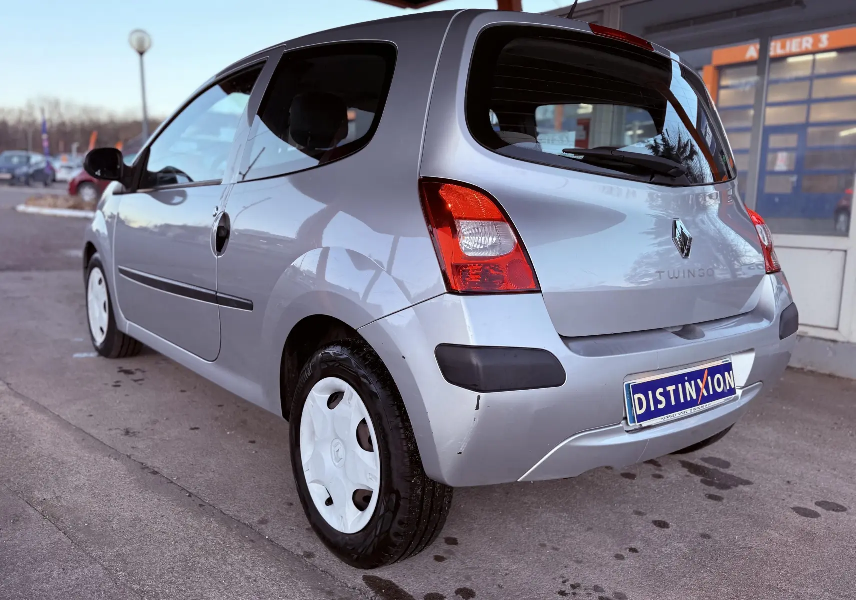 Vue 3/4 arrière gauche d'une Renault Twingo II gris clair avec jantes blanches et pare-chocs noirs.
