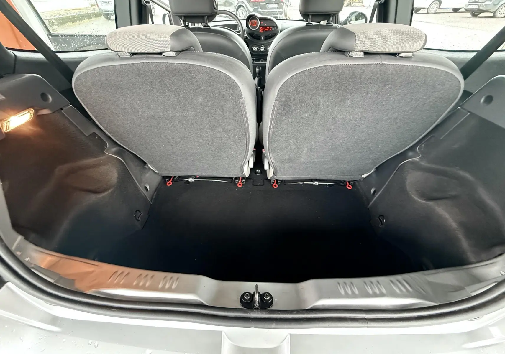 Vue arrière du coffre ouvert d'une Renault Twingo II gris, montrant l'intérieur et les dossiers arrière en tissu gris.