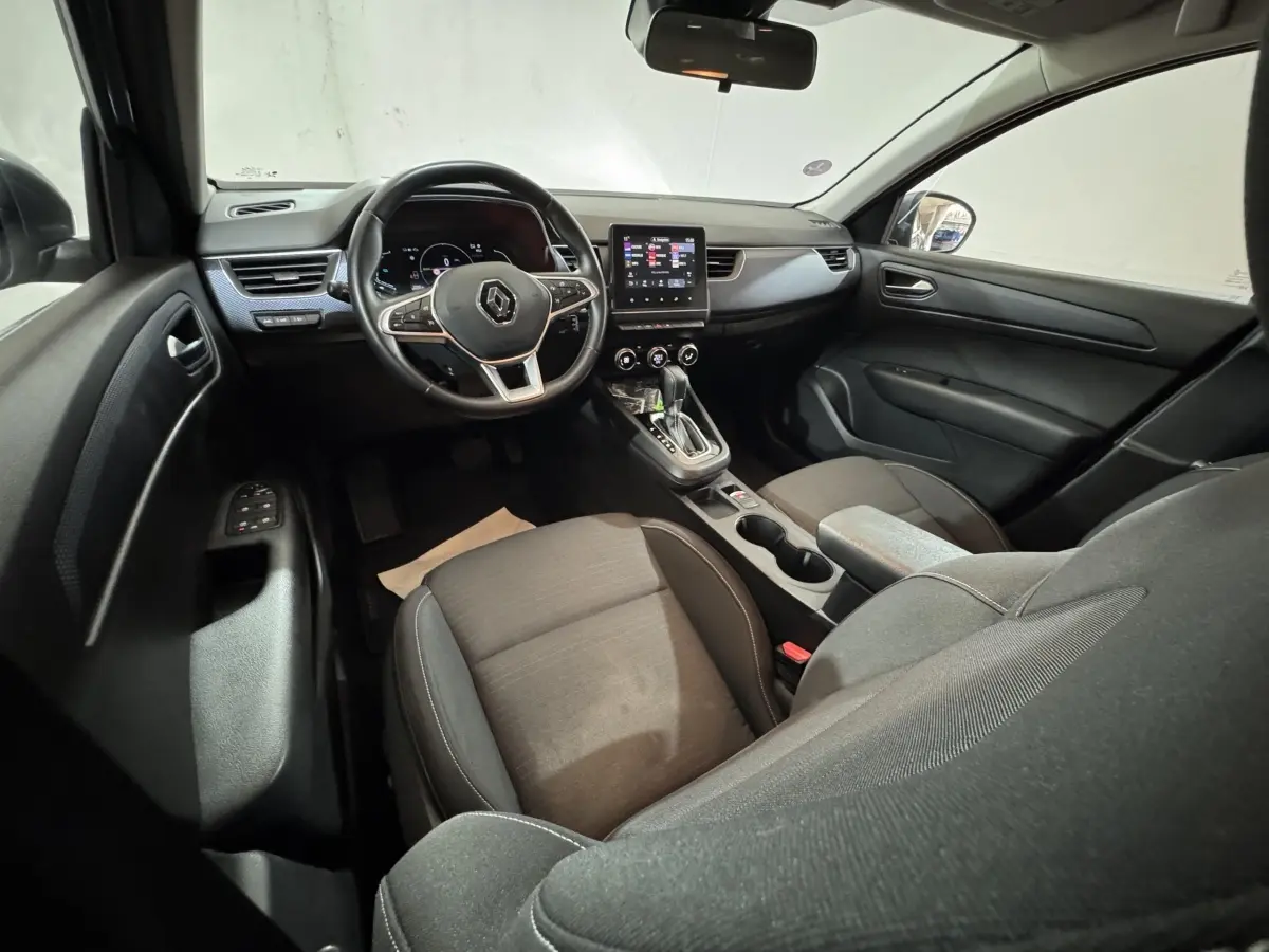 Vue intérieure avant droite du Renault Arkana Business E-TECH 145, tableau de bord noir avec écran tactile central et volant multifonctions.
