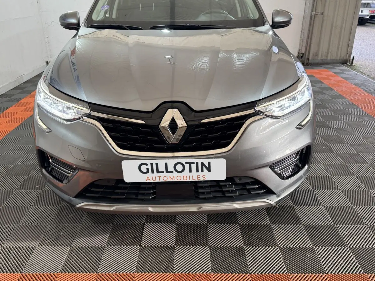 Vue avant rapprochée du Renault Arkana Business E-TECH 145 gris foncé avec phares LED allumés et calandre noire.