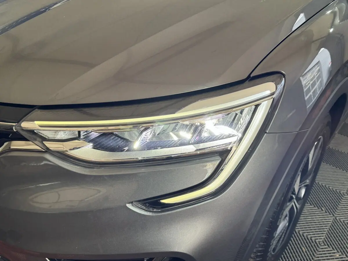 Gros plan sur le phare avant droit LED d’un Renault Arkana Business E-TECH gris foncé, avec partie de la roue visible.