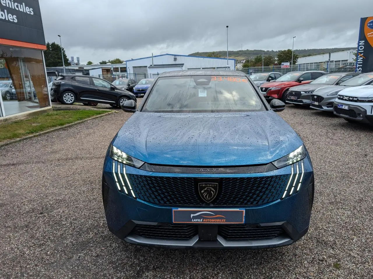 Peugeot 3008 GT bleu métallisé vue de face sous la pluie avec feux LED griffes allumés et calandre noire.