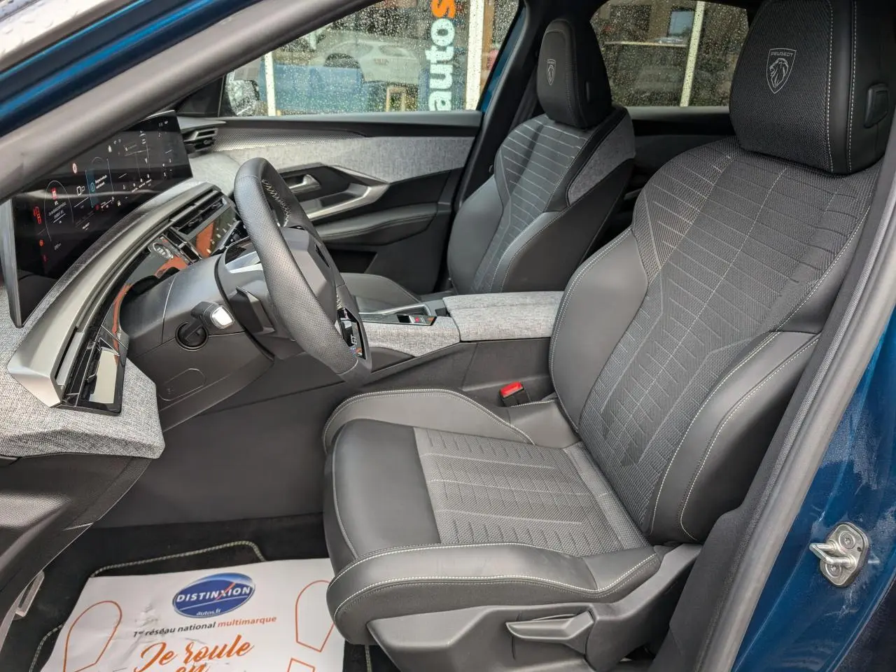 Vue intérieure côté conducteur du Peugeot 3008 GT hybride 2025, sièges tissu et cuir gris, détails tissu Rimini chiné.