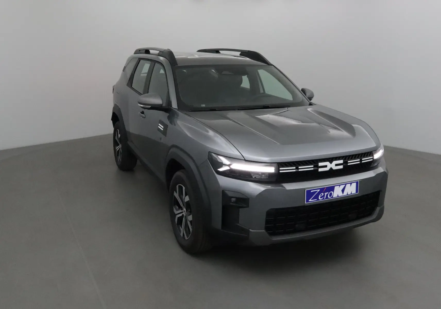 SUV Dacia Bigster gris schiste vu en 3/4 avant droit avec calandre moderne et feux LED allumés.