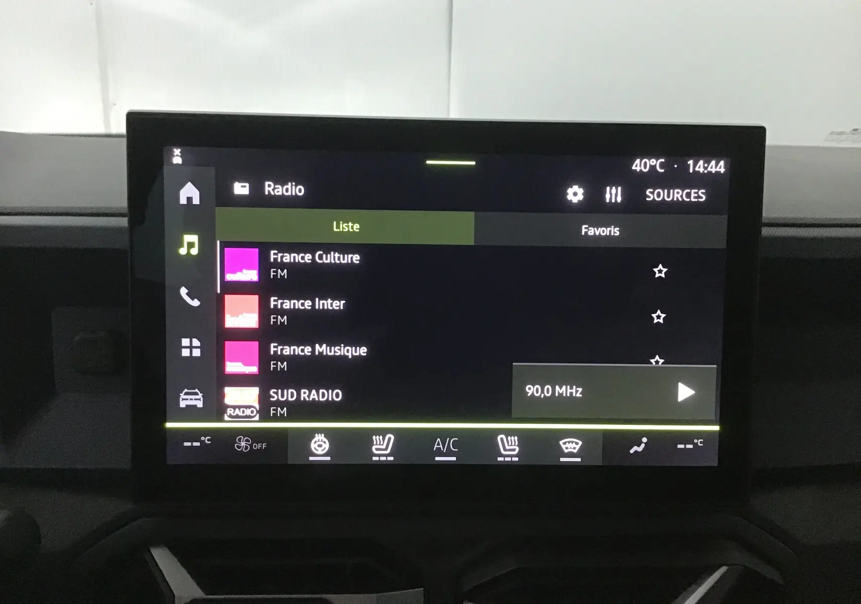 Écran tactile central du tableau de bord du Dacia Bigster gris schiste, affichant les stations radio FM et commandes climatisation.