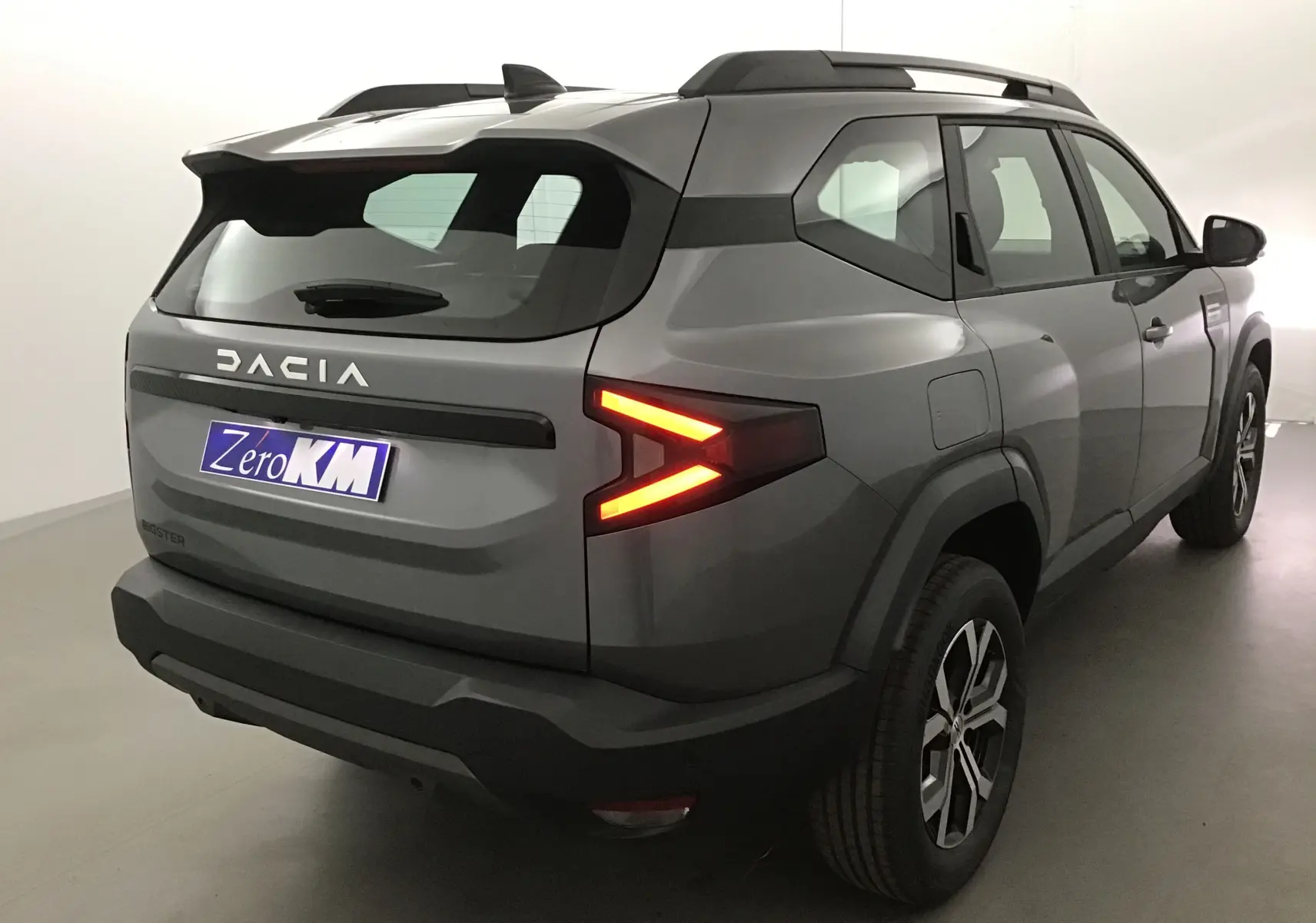 Vue 3/4 arrière droite du Dacia Bigster gris schiste avec feux arrière allumés et jantes alliage 17 pouces.