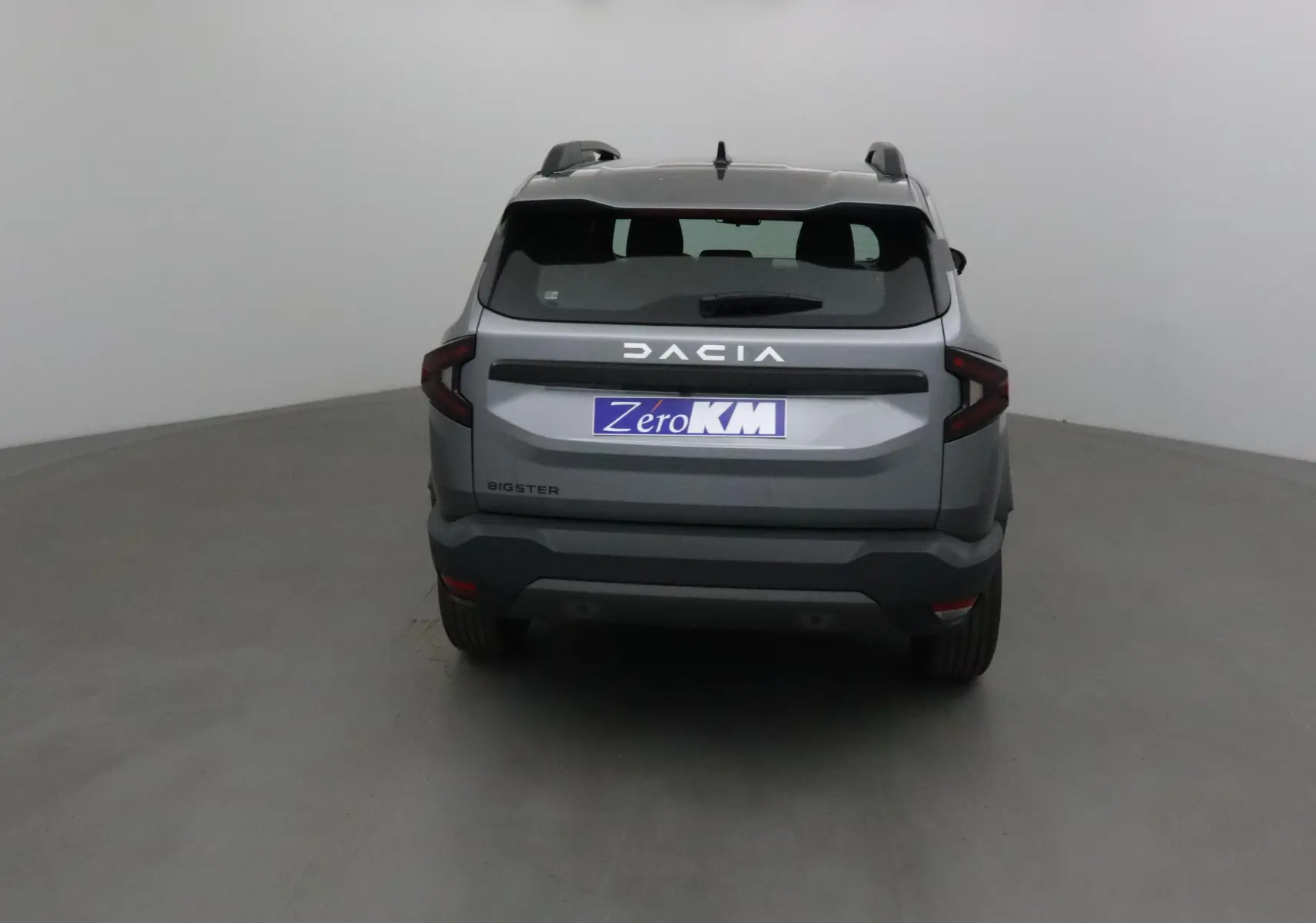 Vue arrière d'un Dacia Bigster gris schiste 2025 avec feux arrière en forme de C et logo lumineux DACIA.