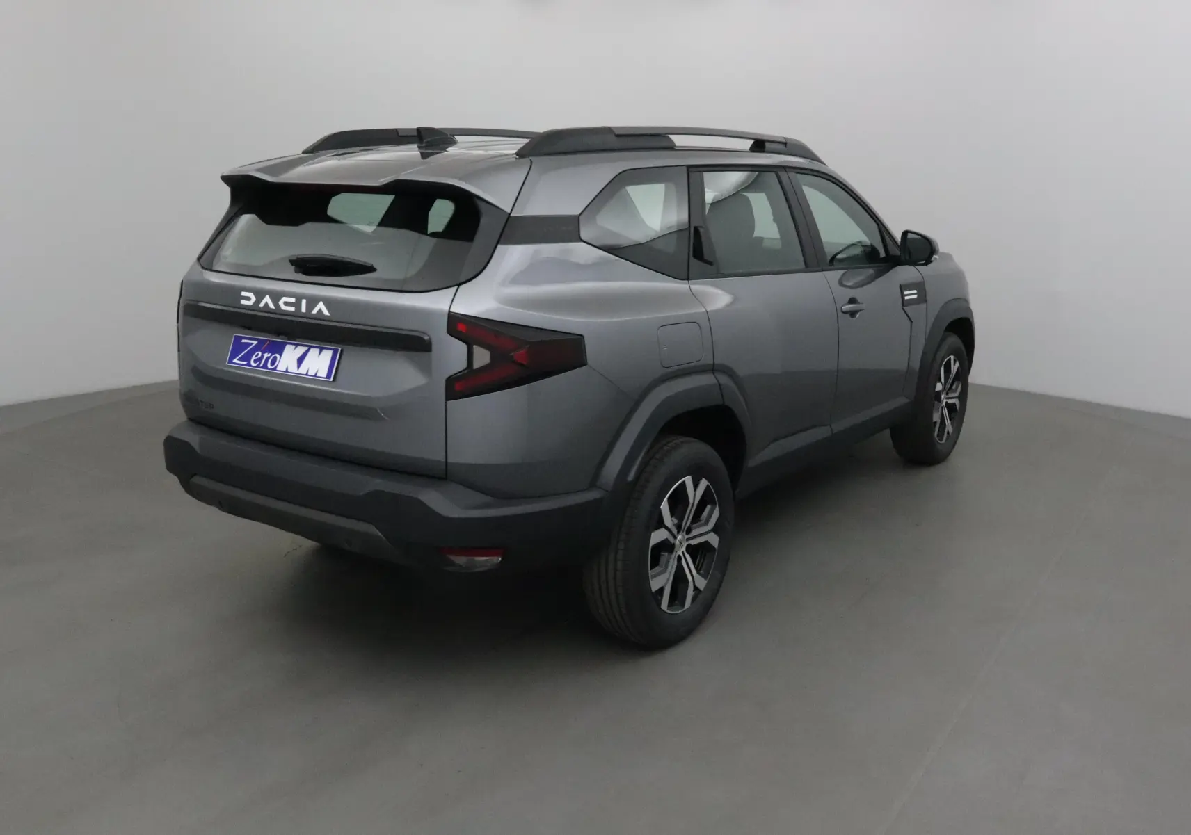 Vue 3/4 arrière droite du SUV Dacia Bigster gris schiste avec barres de toit et feux arrière en forme de flèche.