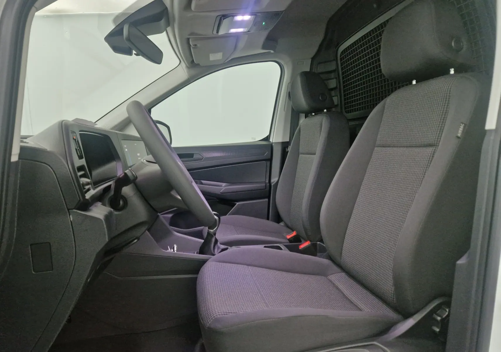 Vue intérieure côté conducteur du Volkswagen Caddy Maxi blanc 2025, sièges avant gris et cloison métallique arrière.