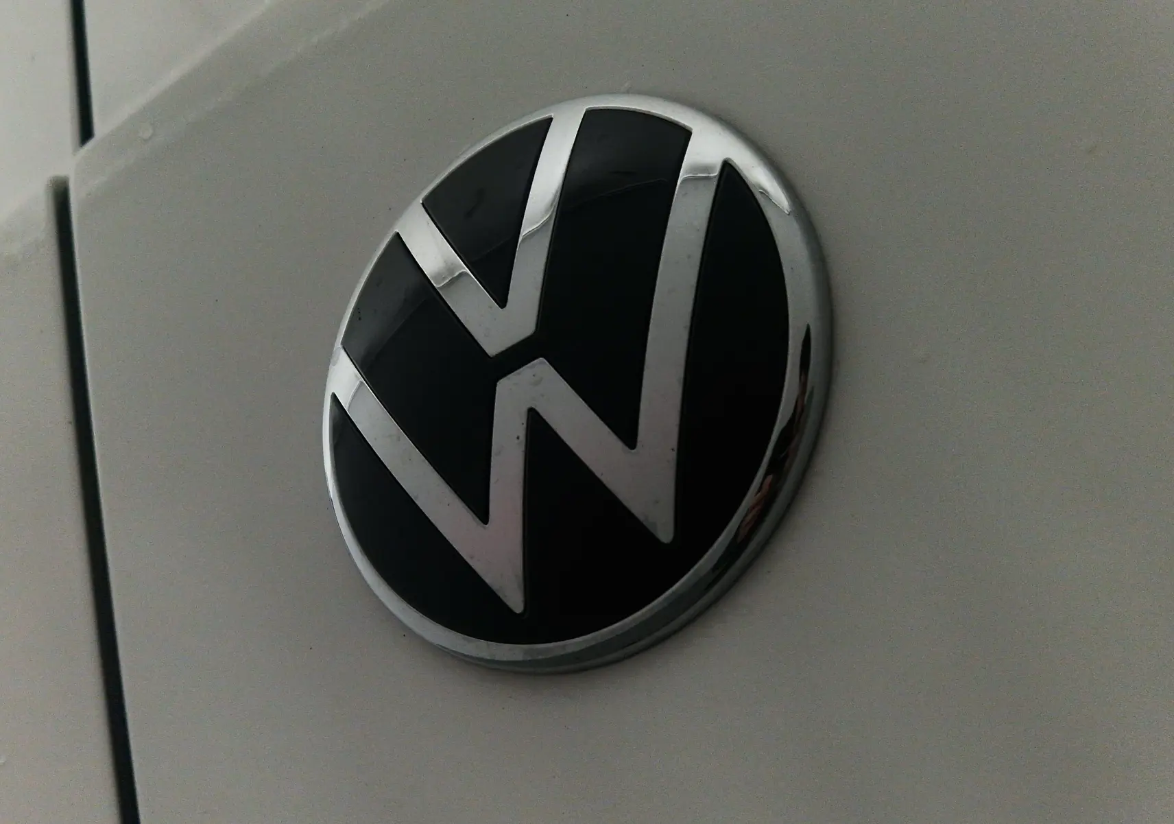 Gros plan sur le logo Volkswagen noir et chrome sur la carrosserie blanche du Volkswagen Caddy Maxi 2025.