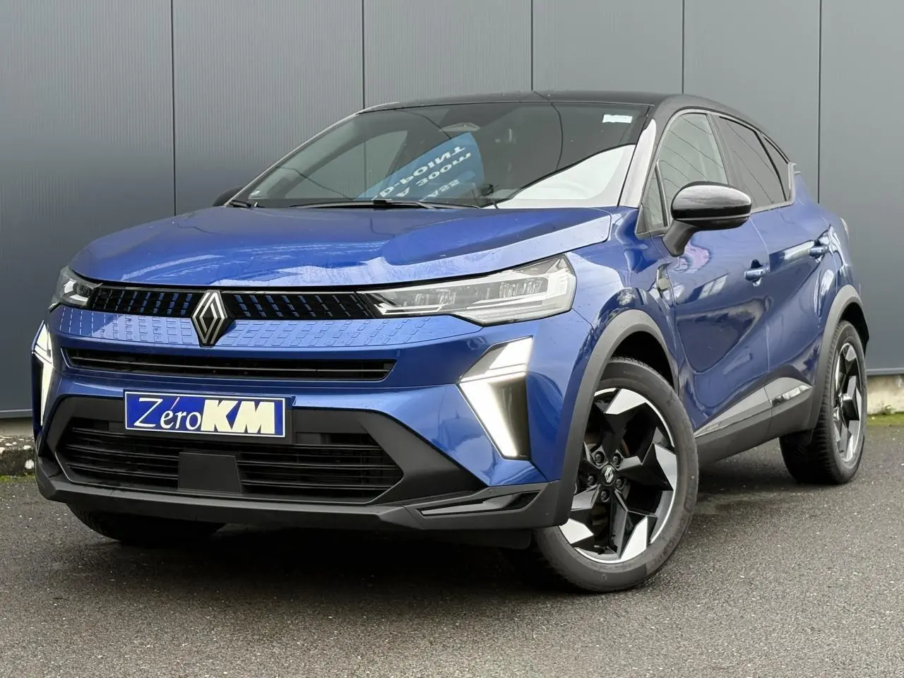 Renault Captur 2025 bleu Iron en 3/4 avant droit avec jantes aluminium noires et toit biton noir.