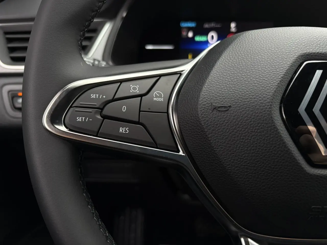 Gros plan sur les commandes à gauche du volant noir du Renault Captur 2025 hybride, avec logo Renault visible.