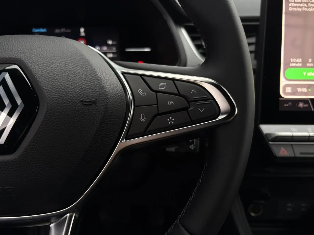 Gros plan sur le volant noir du Renault Captur 2025, avec commandes multifonctions et écran tactile partiel en arrière-plan.