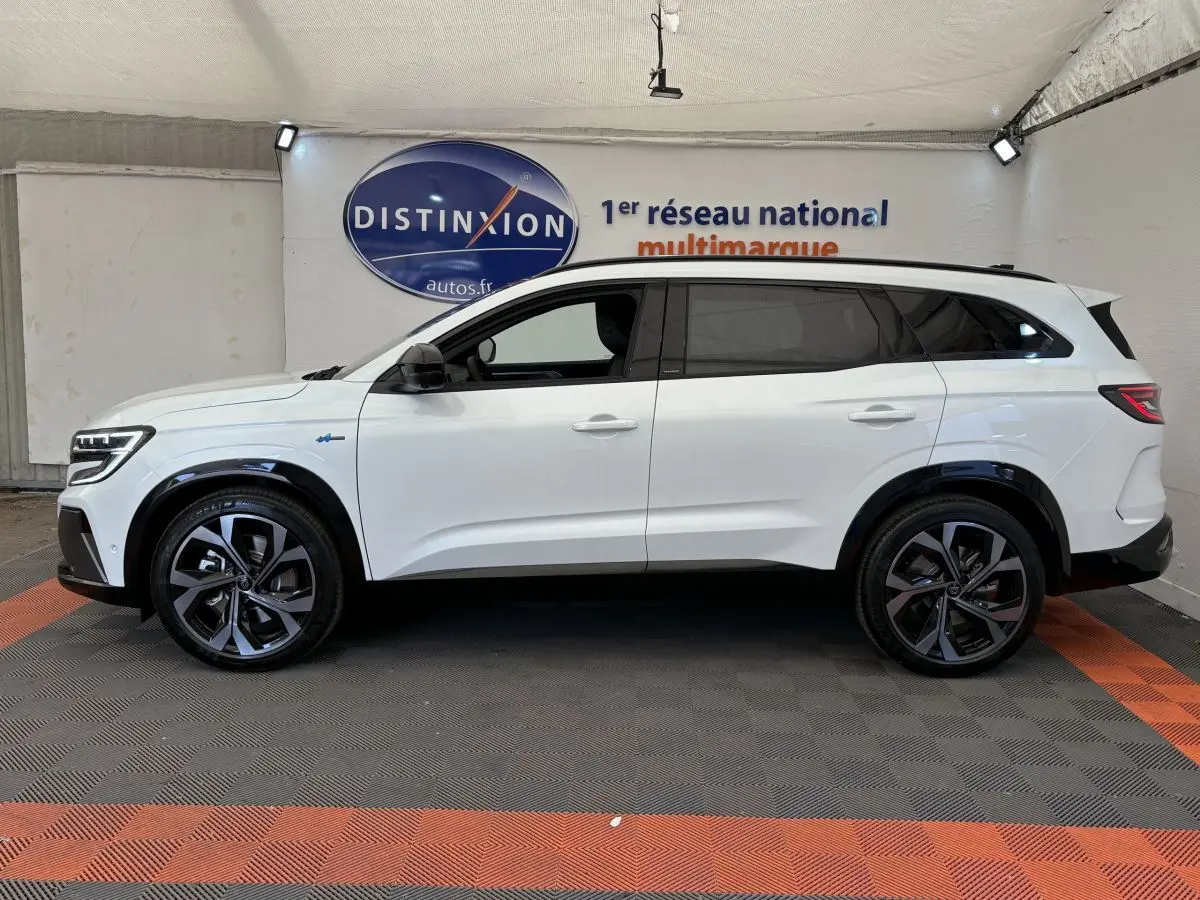 Profil droit d’un Renault Espace blanc esprit Alpine 7 places, avec jantes noires et vitres teintées, en intérieur showroom.