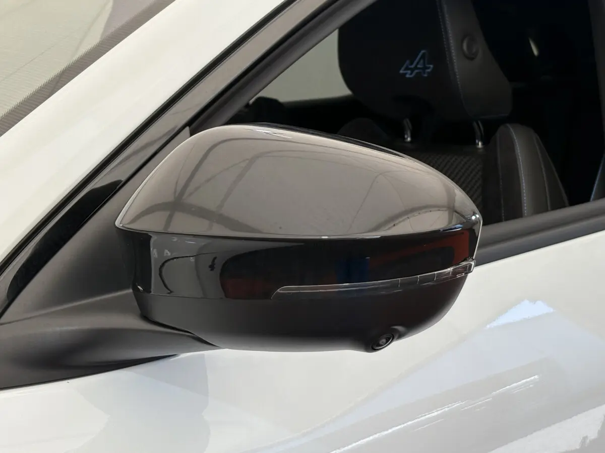 Rétroviseur droit noir brillant d’un Renault Espace blanc esprit Alpine, avec logo Alpine visible sur l’appui-tête.