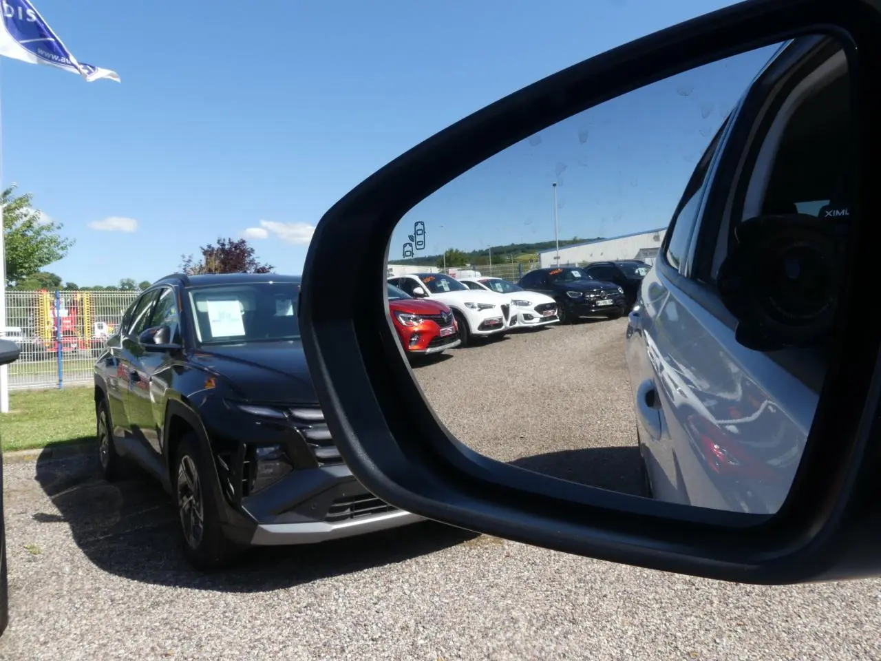 Rétroviseur côté droit montrant un Opel Grandland blanc métallisé en 3/4 arrière sous un ciel bleu.