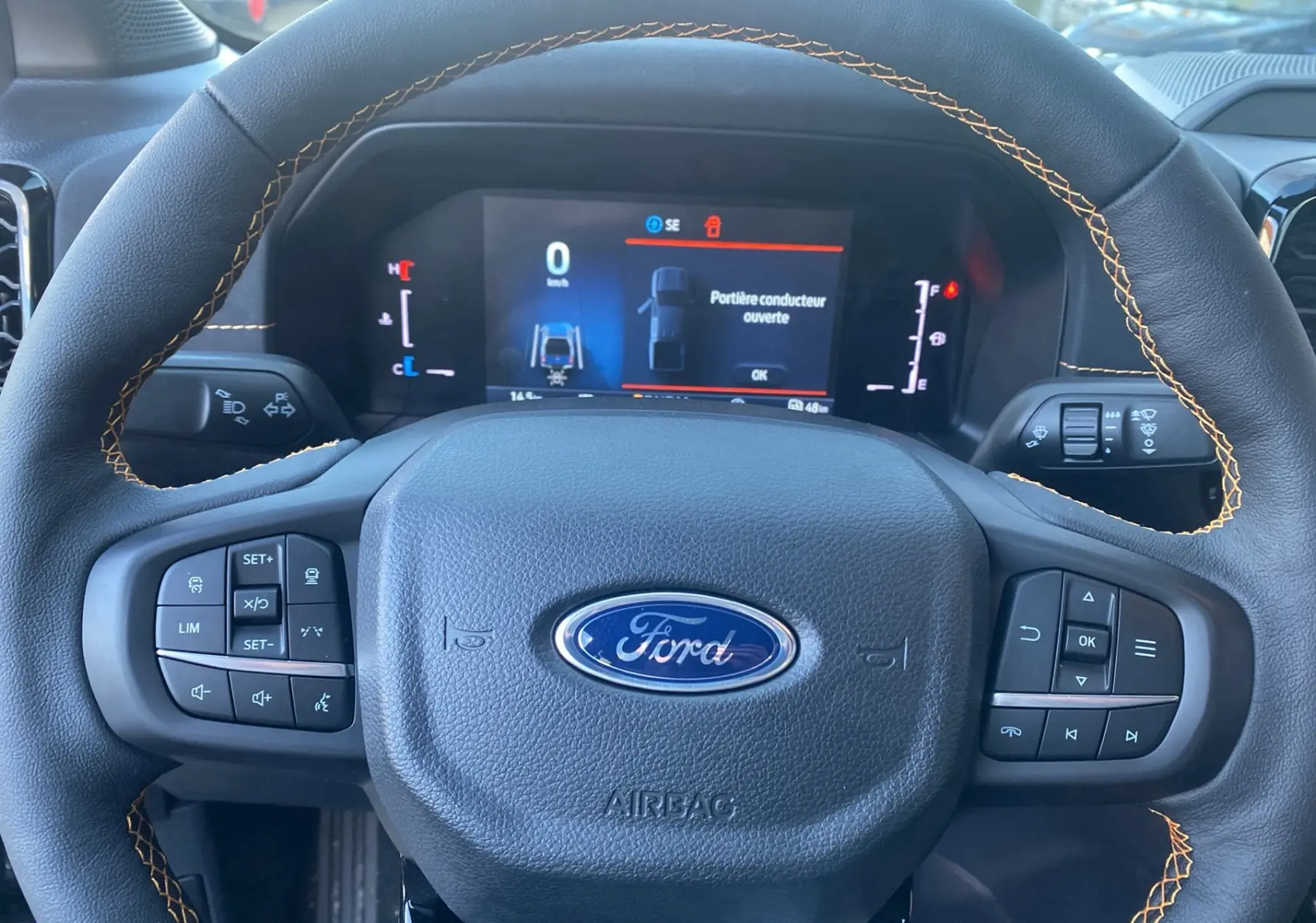 Vue rapprochée du volant cuir noir avec surpiqûres orange et tableau de bord numérique du Ford Ranger gris carbone 2026.