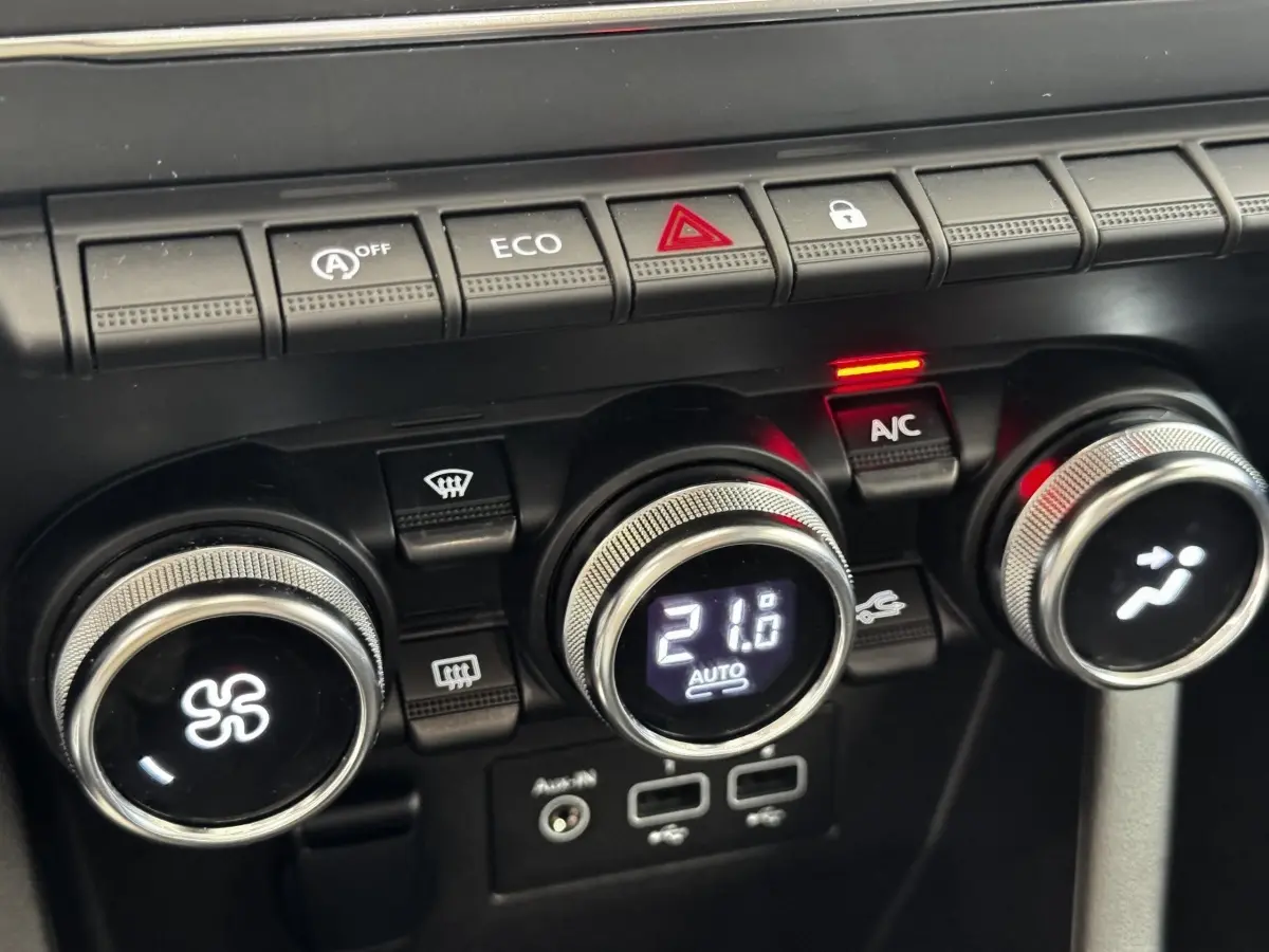 Gros plan sur les commandes de climatisation et boutons de fonction du tableau de bord d’une Renault Clio Business gris clair.