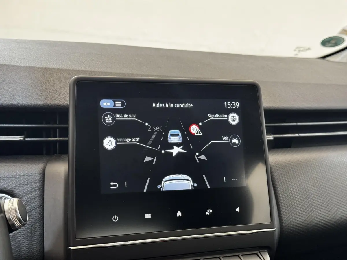Écran tactile central affichant les aides à la conduite dans l’habitacle d’une Renault Clio gris clair, vue de face.