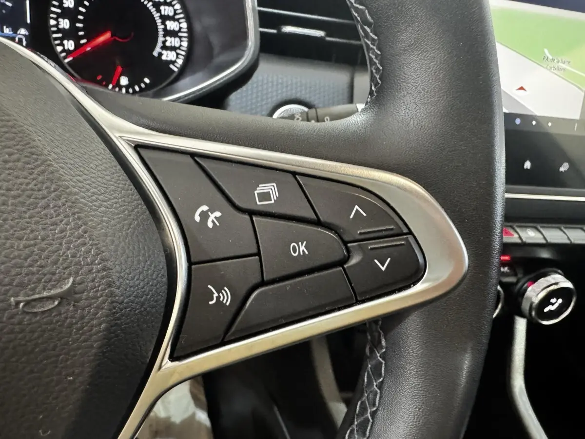 Gros plan sur le volant multifonctions en cuir synthétique de la Renault Clio Business TCe 100, avec commandes vocales et écran tactile visible.