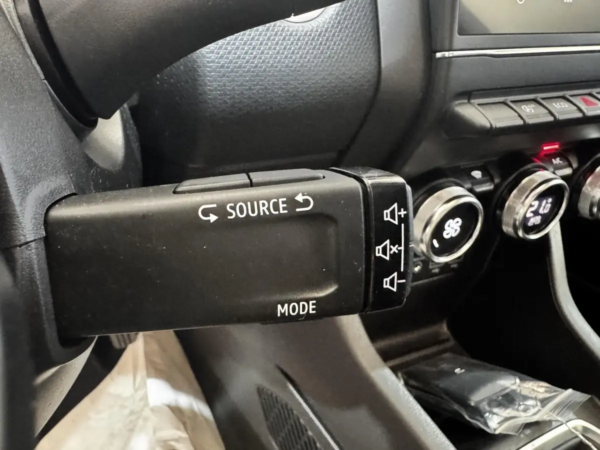 Gros plan sur la commande au volant gauche de la Renault Clio Business TCe 100, avec tableau de bord noir et boutons de climatisation visibles.