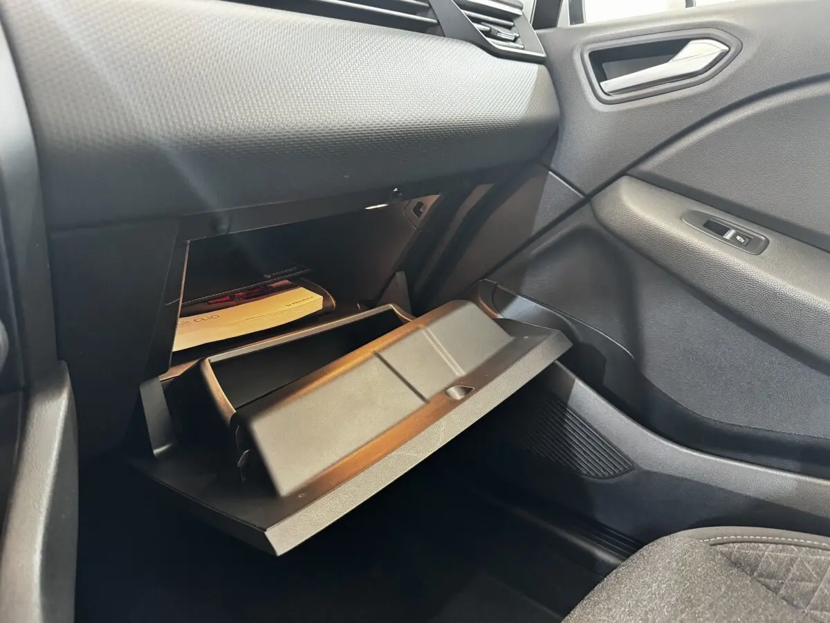 Vue intérieure côté passager de la Renault Clio Business 2020, boîte à gants ouverte avec documents visibles, finition noire.