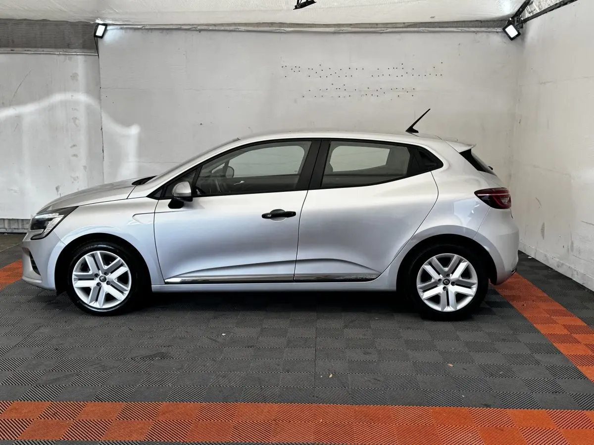 Profil droit d'une Renault Clio Business TCe 100 gris clair 2020, avec jantes alliage et poignées noires, dans un garage.