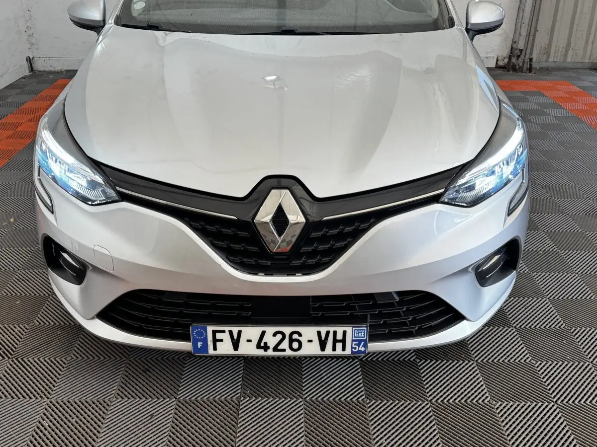 Vue avant rapprochée d’une Renault Clio Business TCe 100 gris clair avec phares LED allumés et calandre noire.