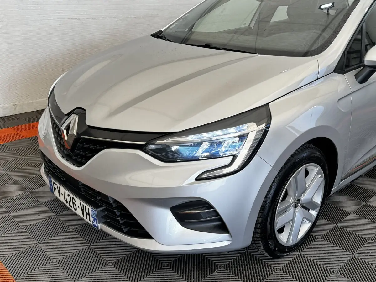 Vue 3/4 avant droit d'une Renault Clio Business TCe 100 gris clair avec phares LED et jantes alliage.